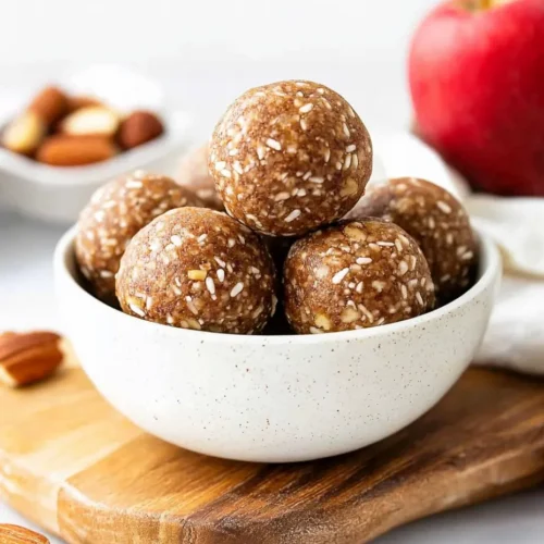 Bowl of healthy no-bake apple pie energy balls with oats, apples, and cinnamon on a wooden board